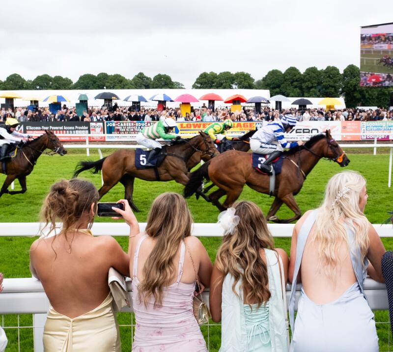 Racegoers at the trackside at Worcester Racecourses, cheering as horses run past