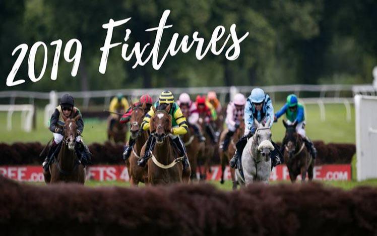 A field of runners heading towards a fence at in the foreground at Worcester Racecourse.