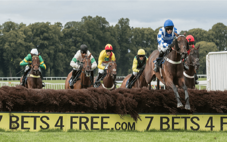 A field of runners jumping over a fence