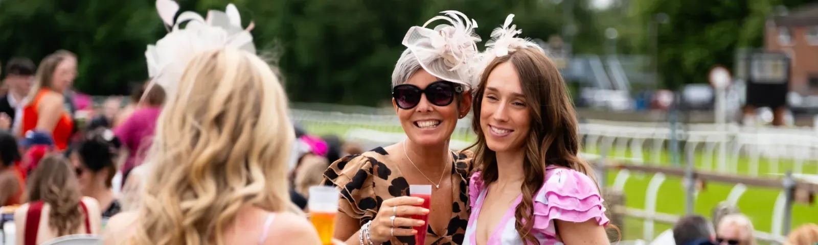 Two ladies dressed for the races pose for a picture in front of the track at Worcester Racecourse