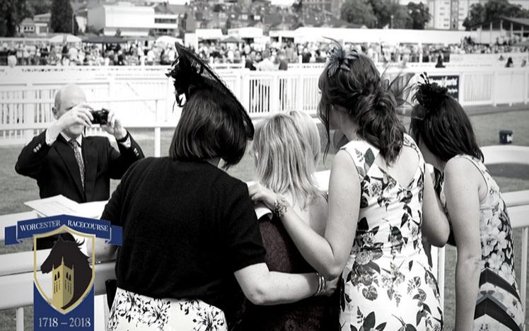 A black and white photograph taken from behind a group of ladies as another photographer can be seen at their front.