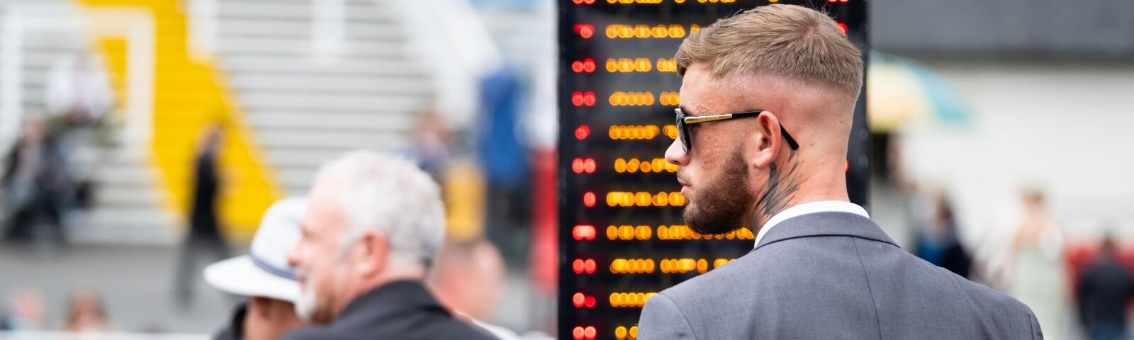 A race goer in a suit in front of a bookmaker board at Worcester Races