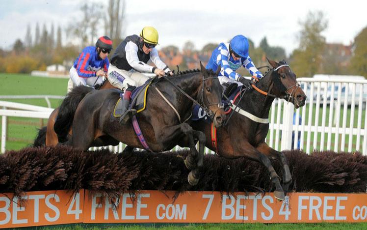 A group of horses jumping a fence at Worcester Racecourse