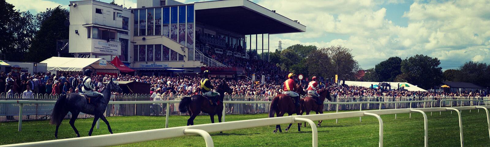Horses racing past the grandstand at Worcester Racecourse.