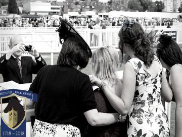 A black and white photograph taken from behind a group of ladies as another photographer can be seen at their front.