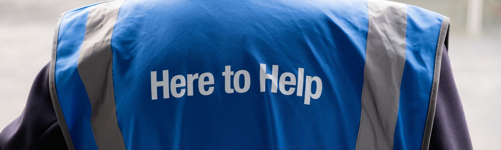 A hi-vis vest that reads Here To Help worn by a steward at Worcester Racecourse