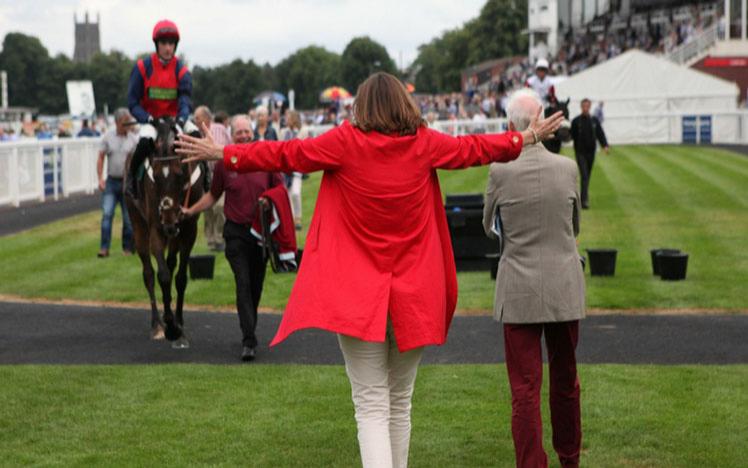 An excited lady walking towards a succesful jockey, horse, and trainer.
