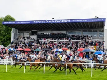 Horses thunder down the track at Worcester Racecourse past a packed grandstand